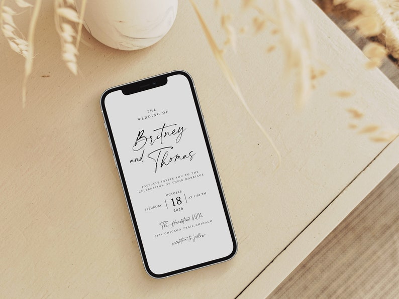 May include: A white smartphone displaying a wedding invitation for Britney and Thomas. The invitation states the wedding will take place on Saturday, October 18, 2022, at 5:00 PM at The Kinzie Hotel, 333 Chicago Trail, Chicago.