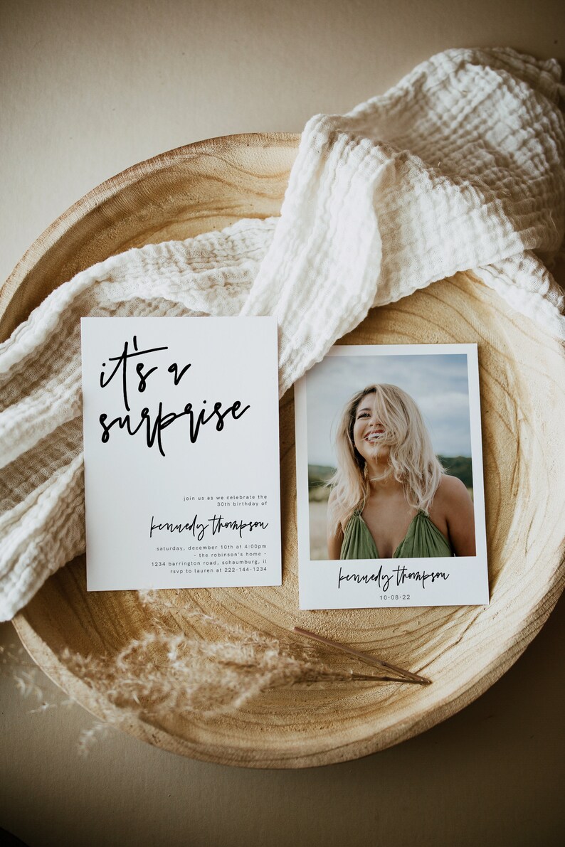 May include: A white card with black calligraphy that reads "it's a surprise" and details for a birthday party. The card is next to a photo of a woman smiling with her hair covering her face. The text on the photo reads "kennedy thompson 10-08-22".