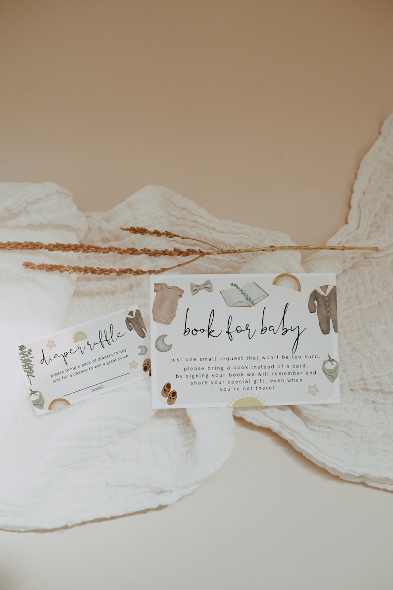 May include: Two baby shower invitation cards with illustrations of baby clothes, moons, and rainbows. One card reads "diaper raffle" and the other says "book for baby". The cards are on a white cloth background.