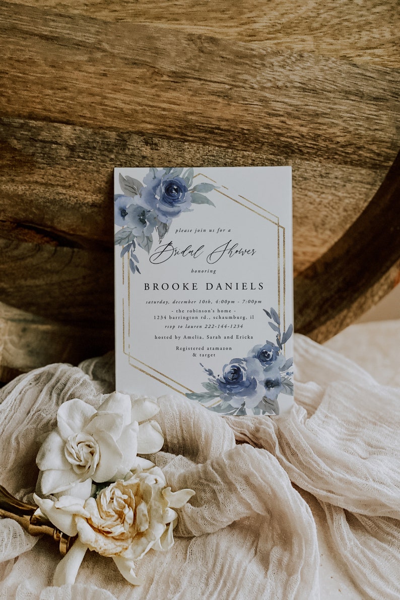 May include: A white invitation with a gold geometric frame and blue watercolor flowers. The text reads "Please join us for a Bridal Shower honoring Brooke Daniels. Saturday, December 10th, 4:00pm - 7:00pm. The Robinson's Home - 1234 Barrington Rd., Schaumburg, IL. RSVP to Lauren 222-144-1234. Hosted by Amelia, Sarah and Ericka. Registered at Amazon & Target."