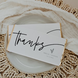 Peut inclure: Barre de chocolat blanc envelopp&eacute;e de papier d'or. La barre comporte un texte noir qui dit "merci" avec un c&oelig;ur et les noms Amelia + Hudson et la date 10-12-20XX.