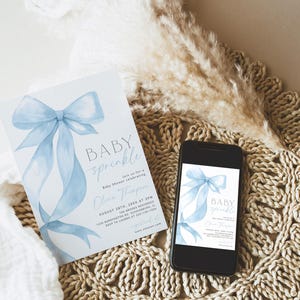 May include: A baby shower invitation and a smartphone displaying the same design. The invitation features a light blue watercolor bow and the words "BABY sprinkle". The phone is on a woven mat with decorative elements.
