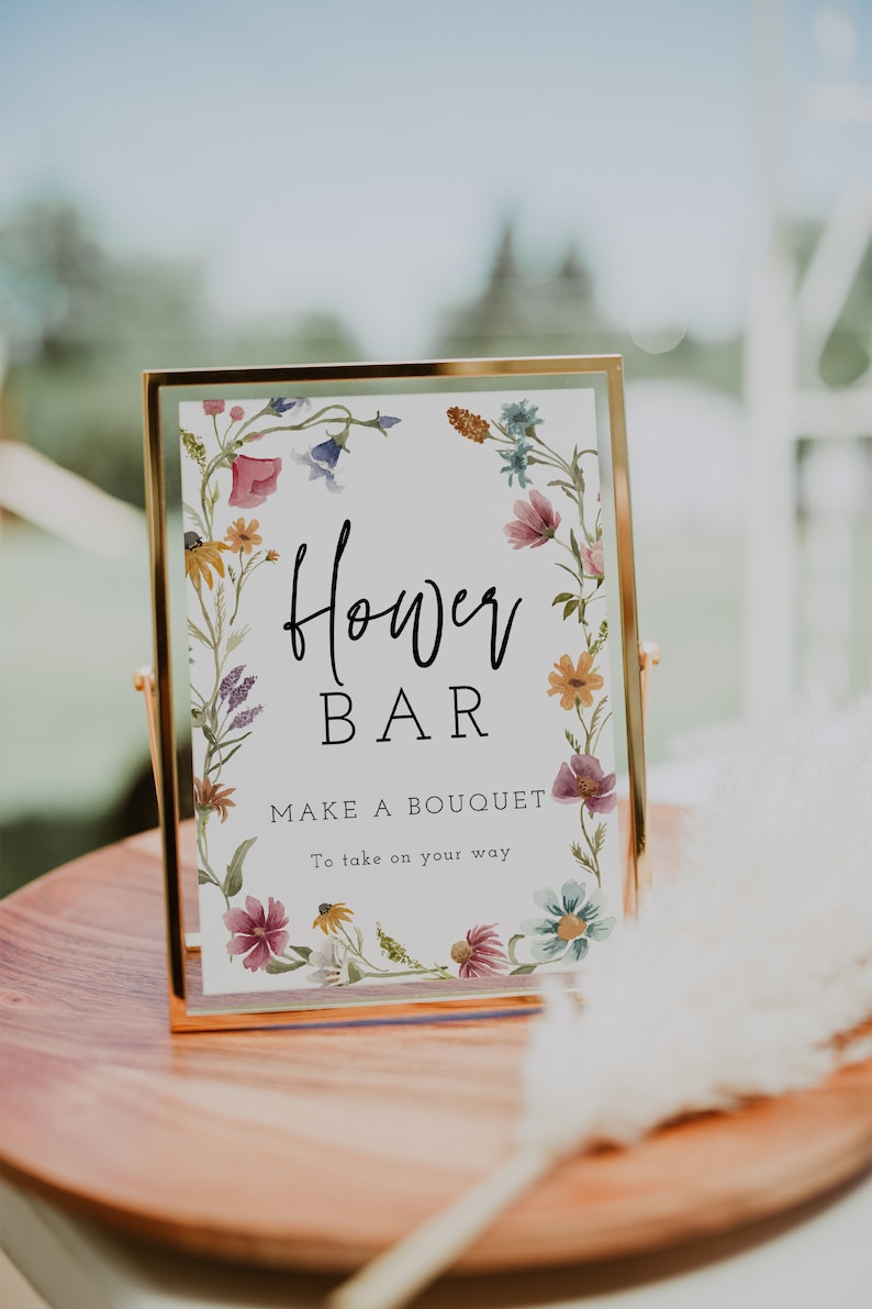 May include: A gold framed sign with a white background and a floral border. The sign says "Flower Bar" and "Make a Bouquet to take on your way".