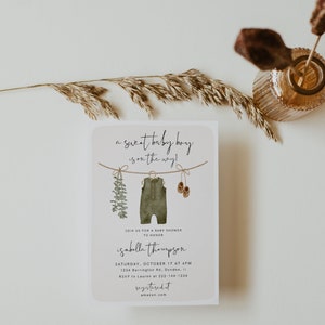 May include: Baby shower invitation with the text "a sweet baby boy is on the way!" The invitation features watercolor illustrations of a onesie, baby shoes, and greenery. The invitation includes the name Isabella Thompson, date, time, and location.