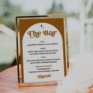 May include: A gold-framed sign with the words "The Bar" in a retro font. The sign lists beer, spirits, wine, and a signature cocktail. The sign is on a wooden surface.