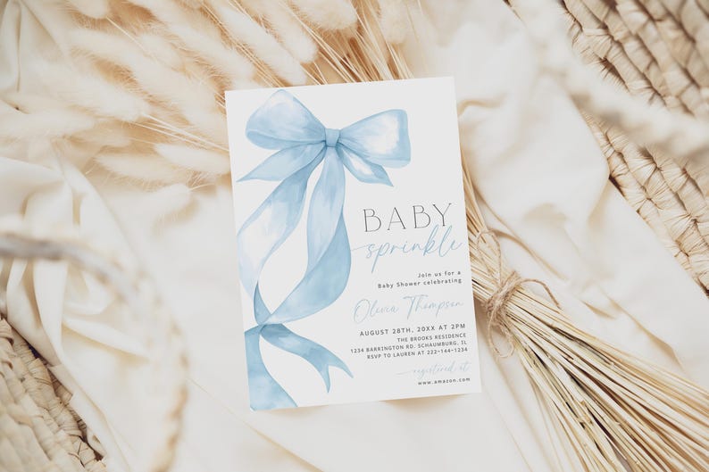 May include: A baby shower invitation card with a light blue watercolor bow and ribbons. The card reads "BABY sprinkle" and includes event details. The invitation is set against a neutral background with dried grasses.