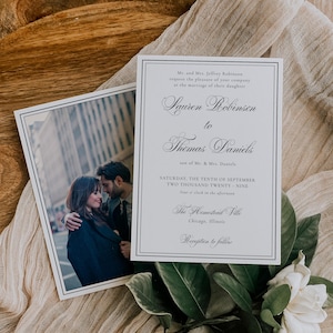 Puede incluir: Invitaci&oacute;n de boda con una foto de una pareja y el texto "Lauren Robinson a Thomas Daniels". La invitaci&oacute;n est&aacute; en una tarjeta blanca con borde negro, con vegetaci&oacute;n y una flor blanca.