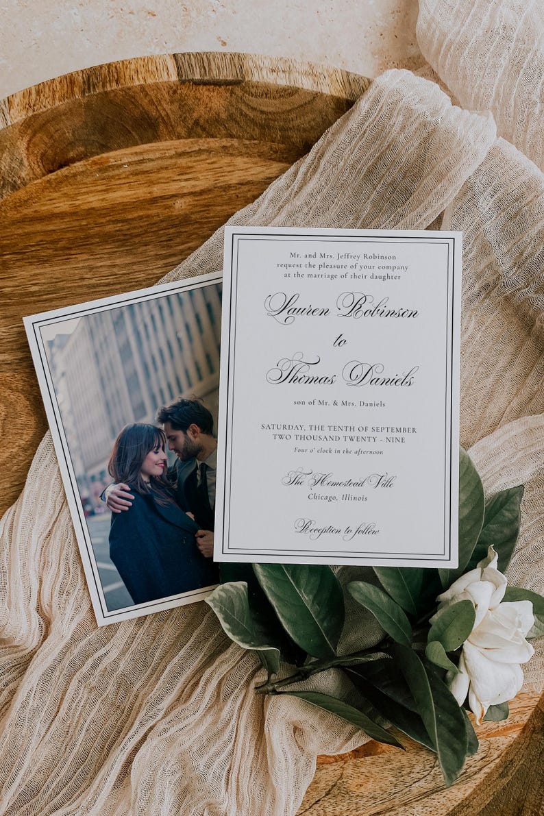 Puede incluir: Invitaci&oacute;n de boda con una foto de una pareja y el texto "Lauren Robinson a Thomas Daniels". La invitaci&oacute;n est&aacute; en una tarjeta blanca con borde negro, con vegetaci&oacute;n y una flor blanca.