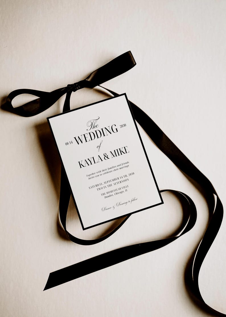 May include: A wedding invitation with black text on a white background, featuring the names Kayla & Mike. The invitation is accented with a black border and tied with a black satin ribbon. The text includes the date, time, and location.