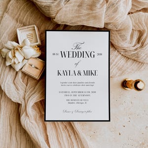 May include: A wedding invitation with the text "The Wedding of Kayla & Mike" in elegant script, set against a neutral backdrop. The invitation is framed in black, with a ring box, flowers, and a gold-toned object nearby.