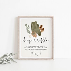 May include: A framed sign with the words "diaper raffle" in elegant script. The sign features watercolor illustrations of baby clothes, including a green onesie, shoes, and a bib. The text below requests guests to leave their card.