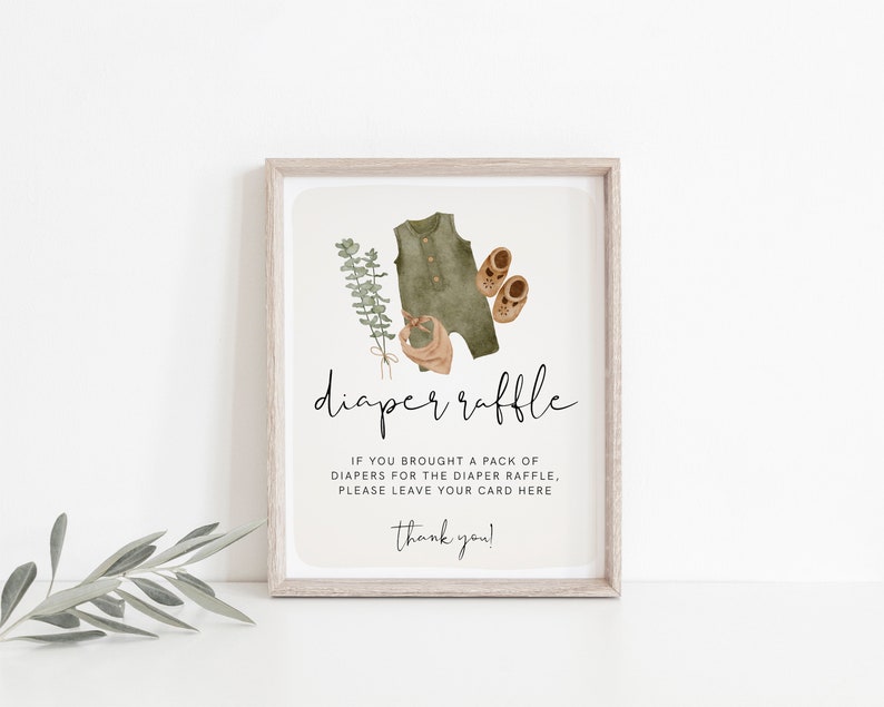 May include: A framed sign with the words "diaper raffle" in elegant script. The sign features watercolor illustrations of baby clothes, including a green onesie, shoes, and a bib. The text below requests guests to leave their card.