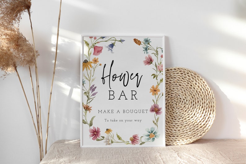 May include: A white sign with a floral border and the text "Flower Bar" in black. Below the text is the phrase "Make a bouquet to take on your way".