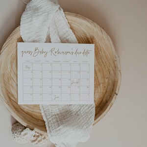 Op de afbeelding: Een witte kaart met een kalender erop. De kalender is voor de maanden mei en juni. De tekst "guess Baby Robinson's due date" staat bovenaan de kaart. Het woord "Due Date" staat in een vakje op de kalender.