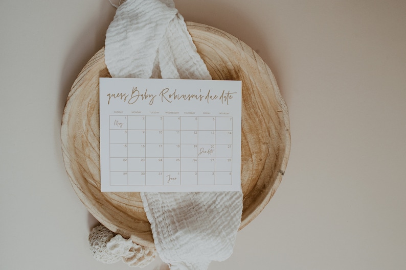 Op de afbeelding: Een witte kaart met een kalender erop. De kalender is voor de maanden mei en juni. De tekst "guess Baby Robinson's due date" staat bovenaan de kaart. Het woord "Due Date" staat in een vakje op de kalender.