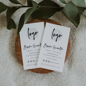 May include: Two white business cards with a simple logo and the name "Brooke Hamilton" printed on them. The text "Owner / Founder" is printed below the name. The cards also include contact information, including an email address, phone number, and social media handles.