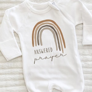 Könnte beinhalten: Weißer Baby-Strampler mit einem braunen Regenbogen und dem Text "Answered Prayer" in brauner Schrift.