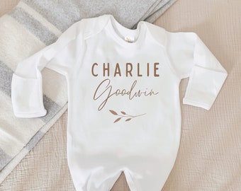 May include: White long-sleeve baby onesie with the name "Charlie Goodwin" written in brown script with a small brown twig design.