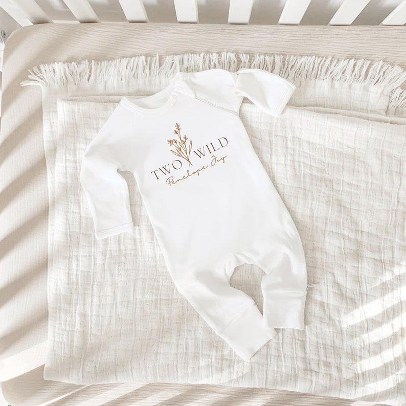 Puede incluir: Mono blanco de manga larga para beb&eacute; con texto marr&oacute;n que dice "TWO WILD Penelope Joy" y un peque&ntilde;o dise&ntilde;o floral.