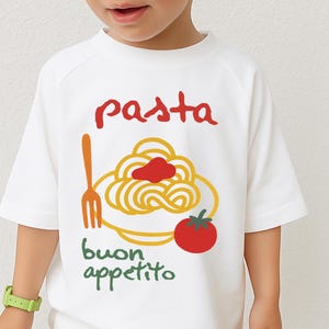Op de afbeelding: Wit T-shirt met een pasta-thema. Het ontwerp toont het woord "pasta" in het rood, een bord spaghetti met rode saus, een tomaat, een vork en de woorden "buon appetito" in het groen.