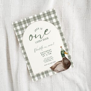 May include: A green and white gingham patterned invitation with a white arch. The text reads "Jack is one lucky duck. Waddle on over! Saturday Nov 12th at 3 PM. The Taylor's 123 Waddle Way Ducktown, FL RSVP 123.456.7880". A cartoon duck wearing a party hat is in the bottom right corner.