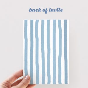 May include: A rectangular invitation card with a blue and white striped design. The text "back of invite" is written in blue script at the top. The card is held by a hand against a white background.