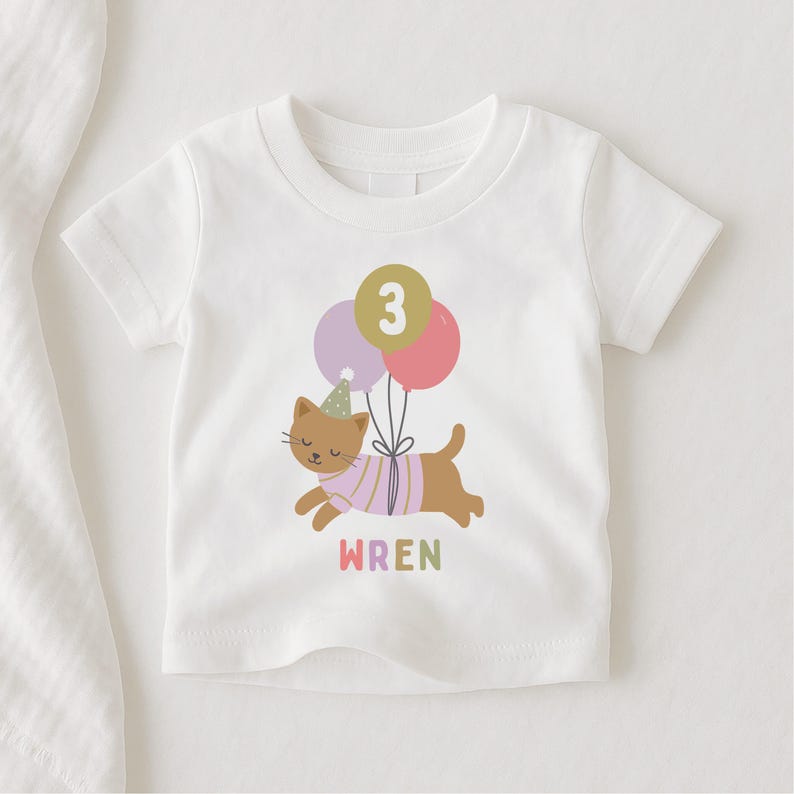 May include: White t-shirt featuring a cartoon cat wearing a party hat and a striped shirt, holding balloons with the number 3. The name "WREN" is printed in colorful letters below the cat. A cute birthday-themed design.