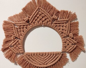 May include: A large, round macrame wall hanging with a brown color. The hanging is made of knotted cords and has a fringe border.
