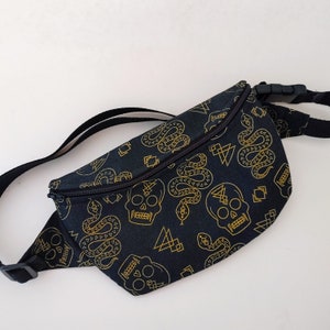 May include: Black fanny pack with a gold snake and skull pattern. The pack has a zipper closure and an adjustable strap.
