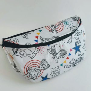 Puede incluir: Ri&ntilde;onera blanca con una cremallera negra y un estampado colorido de personajes de Toy Story. Los personajes est&aacute;n delineados en negro y rellenos de varios colores. El estampado incluye a Woody, Buzz Lightyear, Jessie, Slinky Dog, Rex y Hamm.