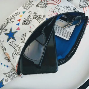 Puede incluir: Una bolsa blanca con cremallera con un estampado de dibujos animados de un perro, estrellas y fuegos artificiales. La bolsa est&aacute; abierta y contiene unas gafas de sol negras, un tel&eacute;fono inteligente negro y una tarjeta de cr&eacute;dito. La tarjeta de cr&eacute;dito tiene el texto "OURE NOT VALID UNLESS SIGNED FDIC, pursuant to a license from Visa U.S.A. Inc.  A 35 &euro; fee will be charged to replace your card after the valid thru date on the front of the card. For activation and PIN, please call and you consent to the cardholder agreement and serviced by Blackhawk Network."