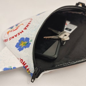 Puede incluir: Una ri&ntilde;onera blanca con cierre de cremallera. La ri&ntilde;onera tiene un estampado floral con flores azules y el texto "Aloha Means Family" en rojo y blanco.