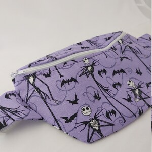 Może przedstawiać: Fioletowa nerka z białym zamkiem błyskawicznym i czarno-białym nadrukiem Jacka Skellingtona i nietoperzy.