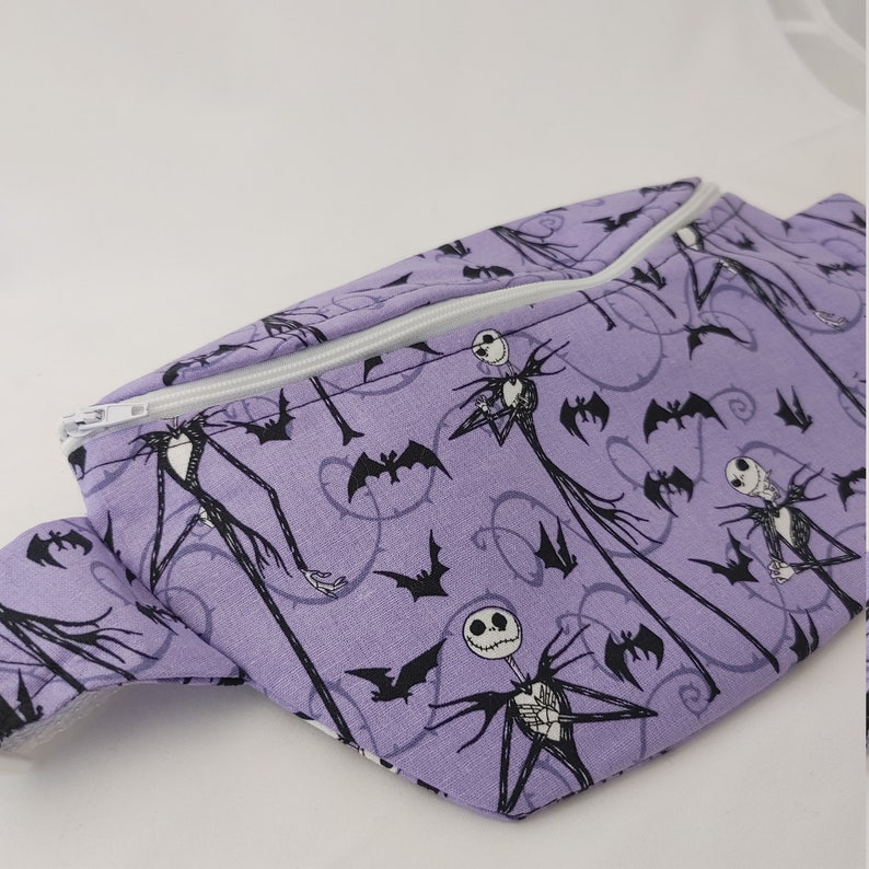 Może przedstawiać: Fioletowa nerka z białym zamkiem błyskawicznym i czarno-białym nadrukiem Jacka Skellingtona i nietoperzy.