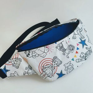 Puede incluir: Una ri&ntilde;onera blanca con una correa ajustable negra. La ri&ntilde;onera tiene un forro azul y est&aacute; decorada con un patr&oacute;n repetido de personajes de dibujos animados de la franquicia Toy Story. Los personajes incluyen a Woody, Buzz Lightyear, Jessie y Bo Peep.