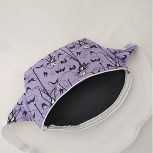 Może przedstawiać: Fioletowa nerka z białym zamkiem błyskawicznym i białym paskiem. Tkanina ma powtarzający się wz&oacute;r czarnych nietoperzy i Jacka Skellingtona z filmu Koszmar przed świętami.