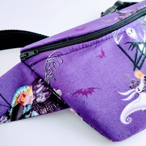 Może przedstawiać: Fioletowa nerka z czarnym zamkiem błyskawicznym i nadrukiem z filmu Koszmar przed świętami z Jackiem Skellingtonem i Sally.