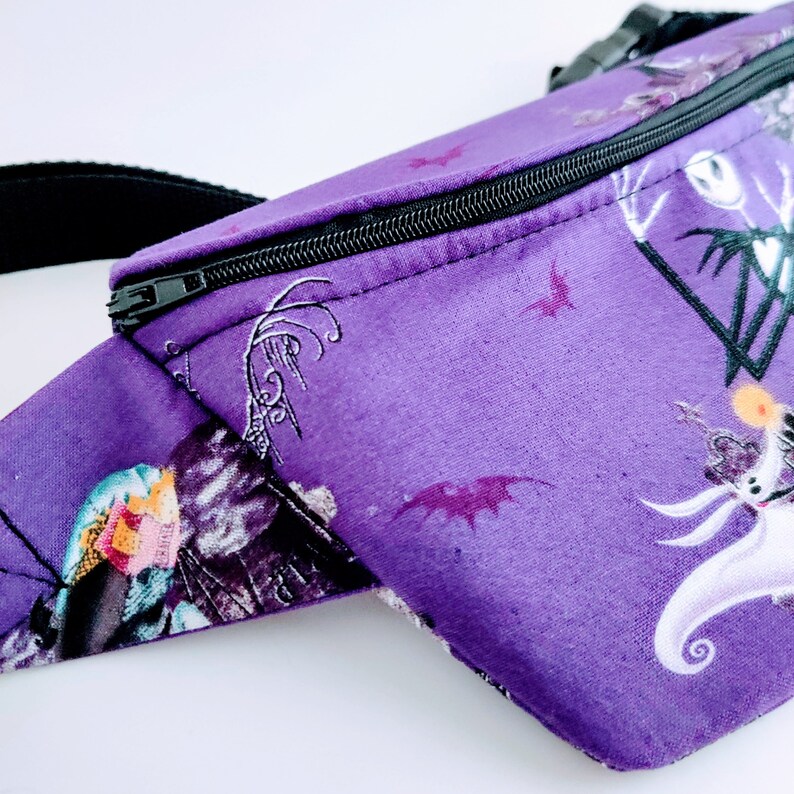 Może przedstawiać: Fioletowa nerka z czarnym zamkiem błyskawicznym i nadrukiem z filmu Koszmar przed świętami z Jackiem Skellingtonem i Sally.