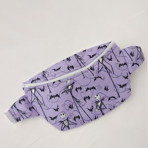 Może przedstawiać: Fioletowa nerka z białym zamkiem błyskawicznym i czarno-białym nadrukiem Jacka Skellingtona i nietoperzy.