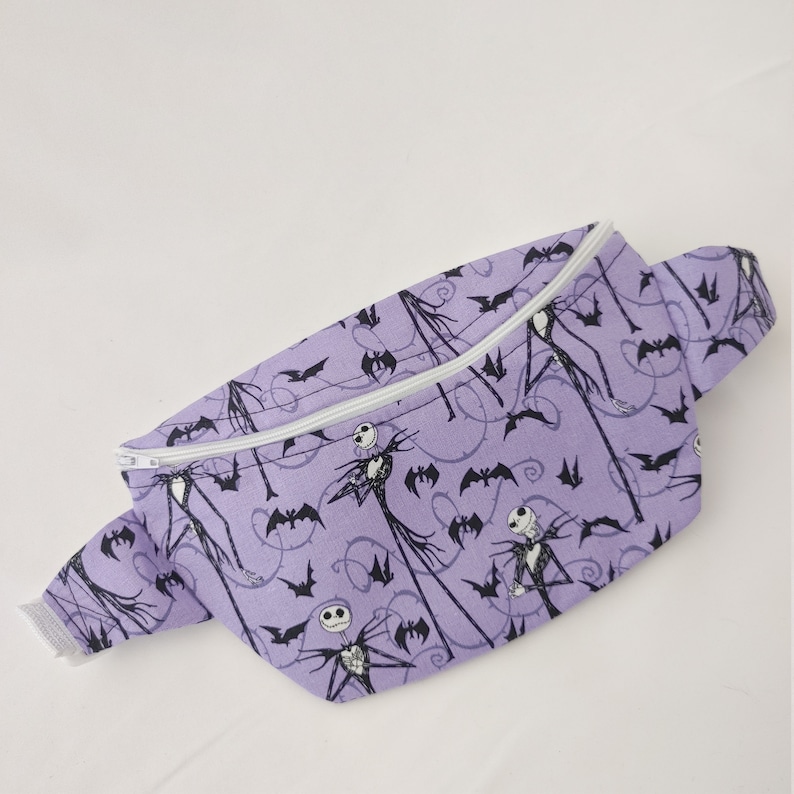 Może przedstawiać: Fioletowa nerka z białym zamkiem błyskawicznym i czarno-białym nadrukiem Jacka Skellingtona i nietoperzy.