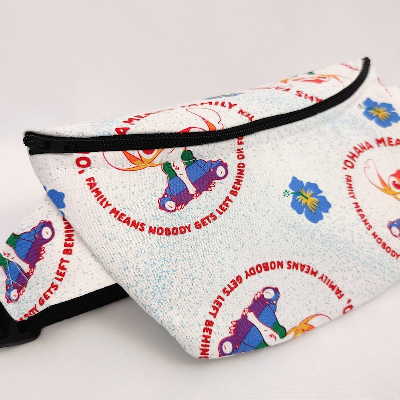 Puede incluir: Ri&ntilde;onera blanca con cremallera negra y un patr&oacute;n repetido de patines de colores y flores. El texto "Ohana Family Means Nobody Gets Left Behind Or Forgotten" est&aacute; impreso en rojo en la bolsa.