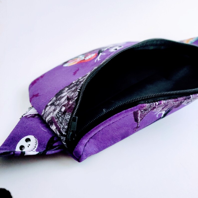 Może przedstawiać: Fioletowa nerka z czarnym zamkiem błyskawicznym i nadrukiem postaci z filmu Koszmar przed świętami.