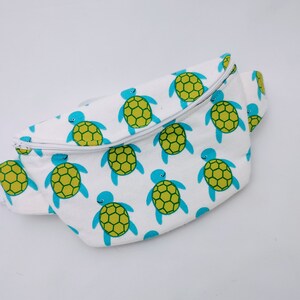 May include: White fanny pack with a zipper closure and a repeating pattern of blue and green sea turtles.