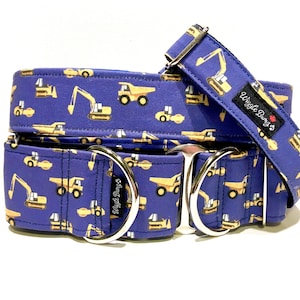 Puede incluir: Un collar de perro azul con estampado de vehículos de construcción. El collar tiene dos anillos en D plateados y el texto "Wiggle Buns" está impreso en el collar.