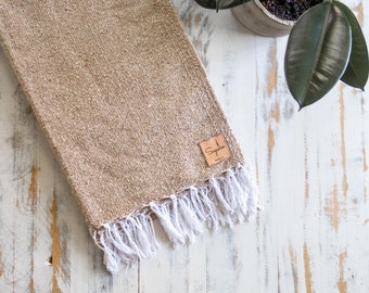 May include: A brown woven throw blanket with white fringe. The blanket has a small leather tag with the word "Sequoia" on it.