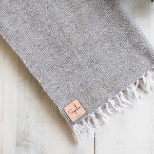 May include: A gray woven throw blanket with a white fringe and a brown leather tag that says "Sequoia" on it.