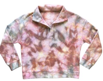 May include: A tie-dye long-sleeve shirt with a collared neckline. The shirt features a waffle knit texture and a color palette of pink, peach, yellow, and blue. The shirt has a relaxed fit and a button-up placket.