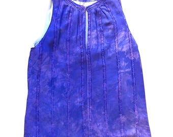 May include: A sleeveless, tie-dye style top in shades of blue and purple. The top features vertical stitched detailing and a keyhole neckline. The fabric appears lightweight and flowing, suitable for warm weather.