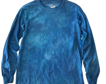 May include: A long-sleeved, crew neck shirt in shades of blue, with a tie-dye pattern. The shirt has a tag attached near the neckline. The fabric appears soft and comfortable, suitable for casual wear.