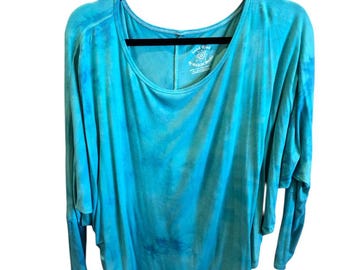 May include: A turquoise tie-dye long-sleeve shirt with a scoop neck and a relaxed fit. The shirt is hanging on a black hanger. The tag reads "good eye" and "Waxon Mauve".